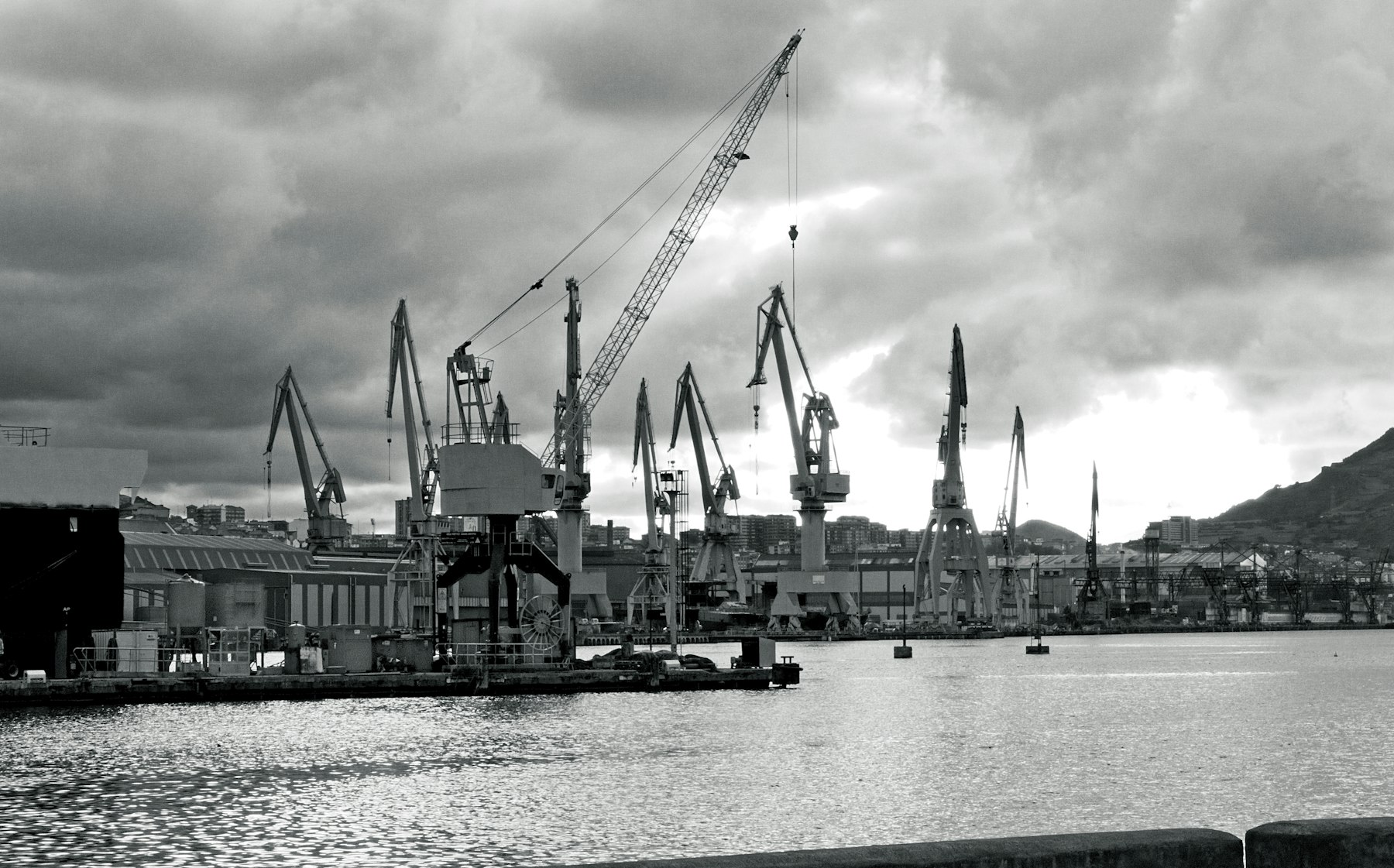 Harbour cranes along an industrial waterfront under a heavy sky